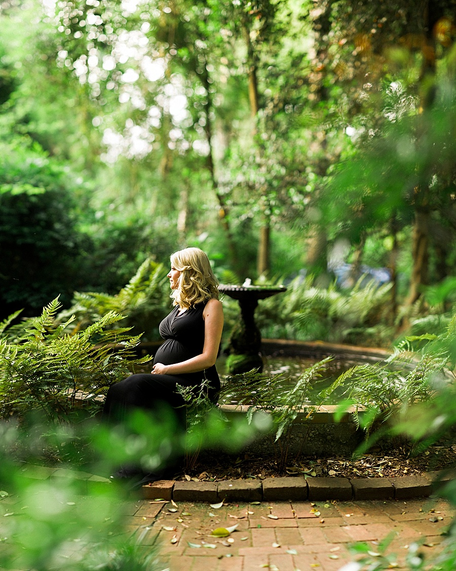 Expectant mother sits on the edge of a fountain at Wing Haven Gardens in Charlotte NC