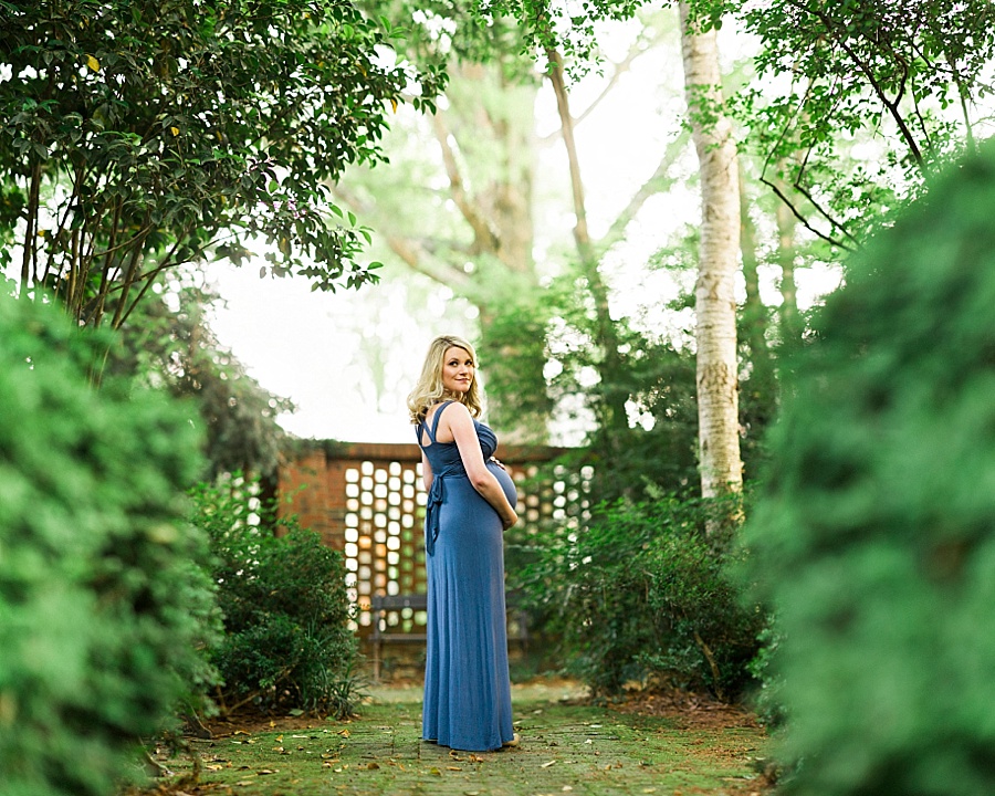 Pregnant mother stands by brick wall at the Wing Haven Gardens in Charlotte NC