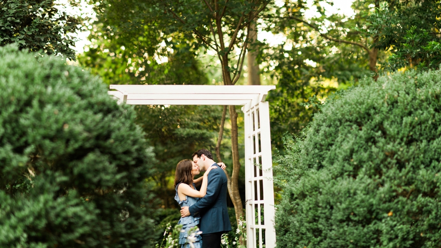 Couple hugging under arbor at Wing Haven Gardens in Charlotte NC