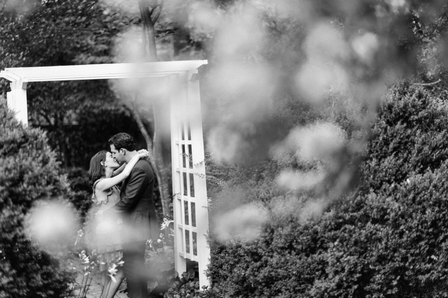 B&W of couple standing under arbor at Wing Haven Gardens in Charlotte NC