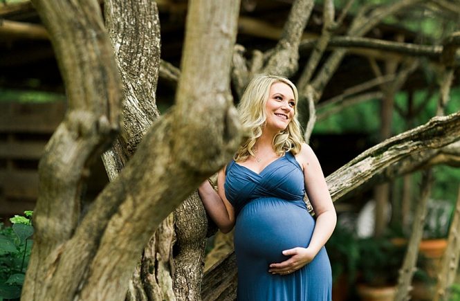 Pregnant woman stands by tree at Wing Haven Gardens in Charlotte NC