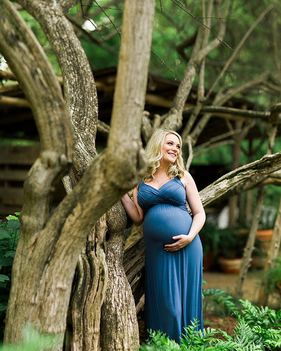 Pregnant woman stands by tree at Wing Haven Gardens in Charlotte NC