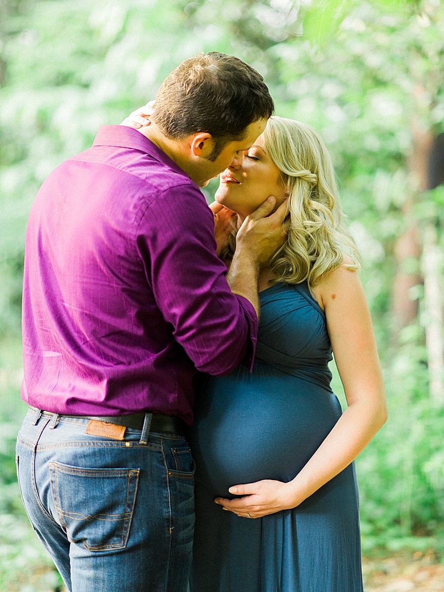 Husband kisses wife during a maternity session at Wing Haven Gardens in Charlotte NC